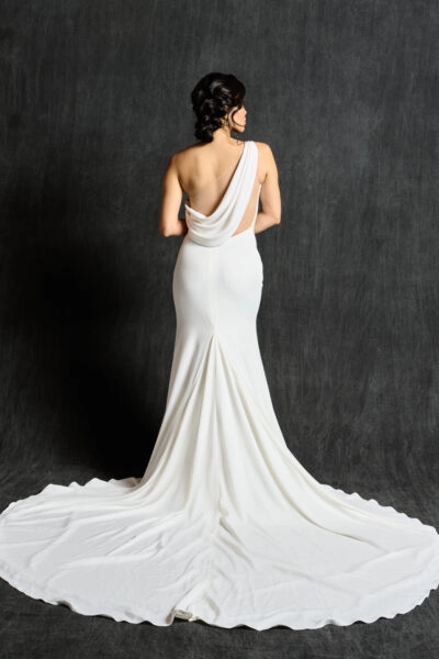 Back view of a woman in a white one-shoulder cowl back wedding dress with a long train.