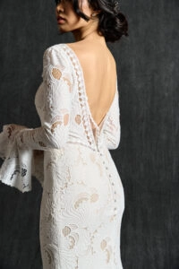 Back view of a boho long sleeve lace wedding dress, featuring a deep V-back with scalloped lace edging and delicate button detailing, showcasing intricate lace patterns and flared sleeve cuffs for a romantic, vintage-inspired bridal look.