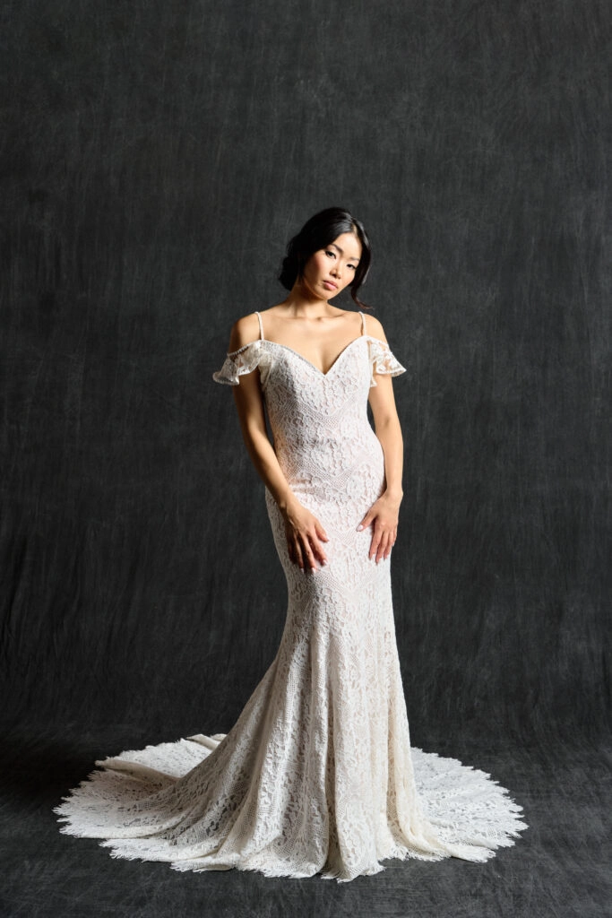 Elegant off-the-shoulder lace wedding dress with a fitted silhouette and flowing train, perfect for a romantic and timeless bridal look.