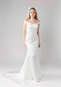 Elegant satin off-the-shoulder wedding dress with a fitted bodice and flowing train, modeled by a bride with a bow headband.