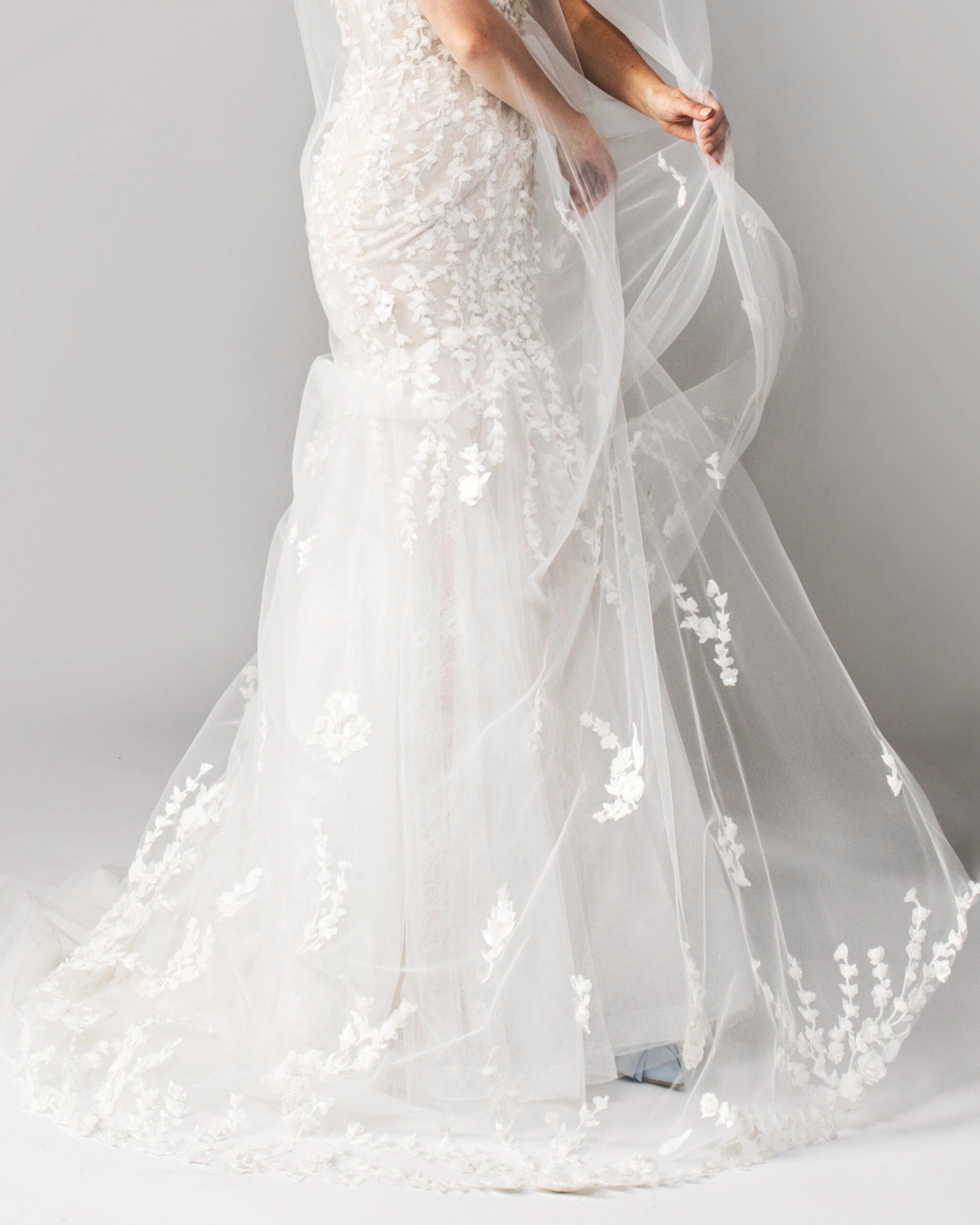Close-up of a lace wedding dress with a 3D floral veil draped over the gown, showing intricate floral details.