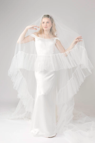 Elegant bride in an off-the-shoulder gown with a long ruffle veil, showcasing a soft and romantic bridal look.