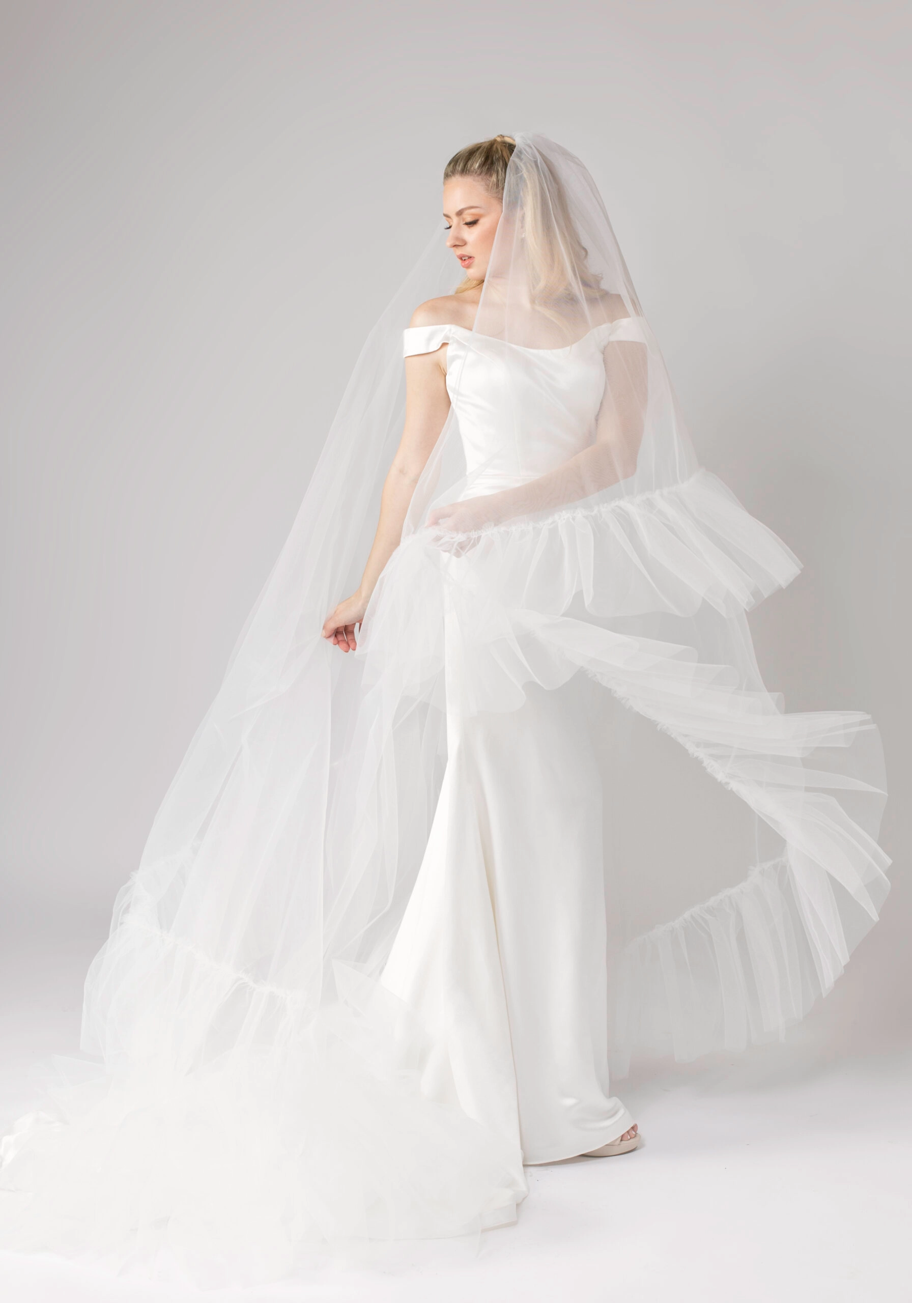 Bride in an elegant off-the-shoulder satin gown and flowing ruffle veil, capturing a timeless and romantic bridal style.
