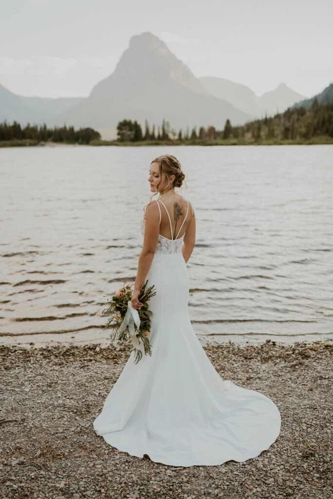 Montana bride in crepe lace dress by water and mountain with wildflower bouquet