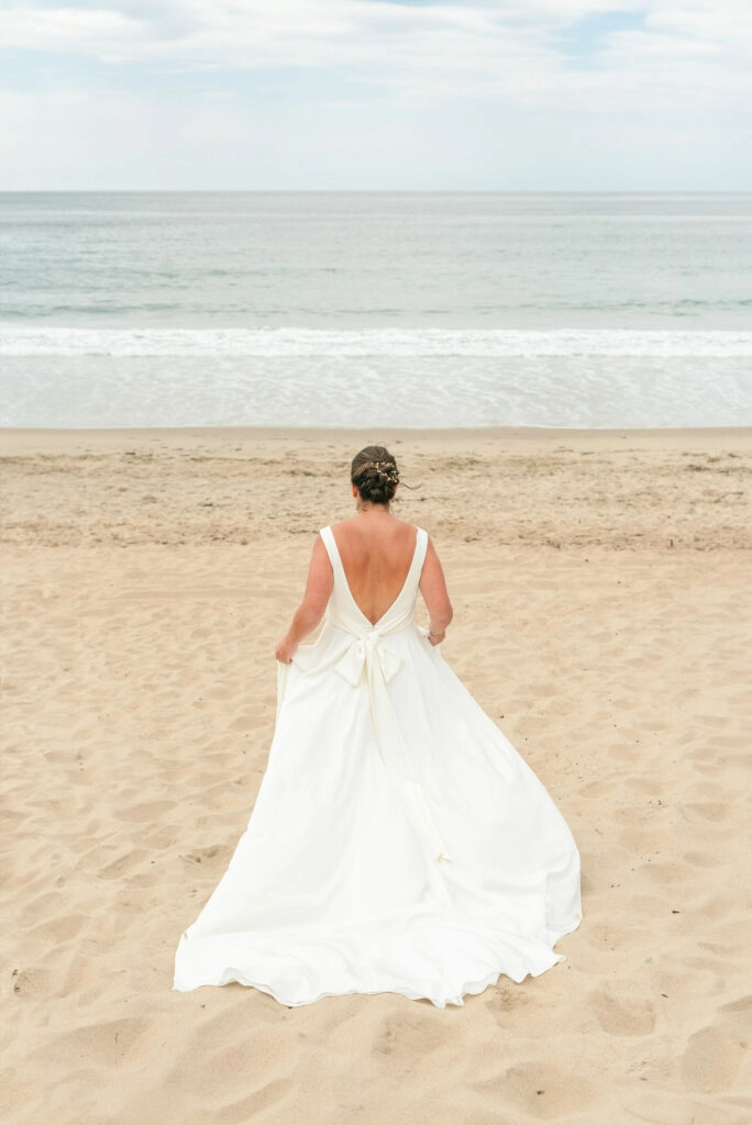 bride running away on beach in ivory crepe dress with low back and long bow